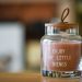A glass jar candle with 'Enjoy the little things' text and wooden lid on table.
